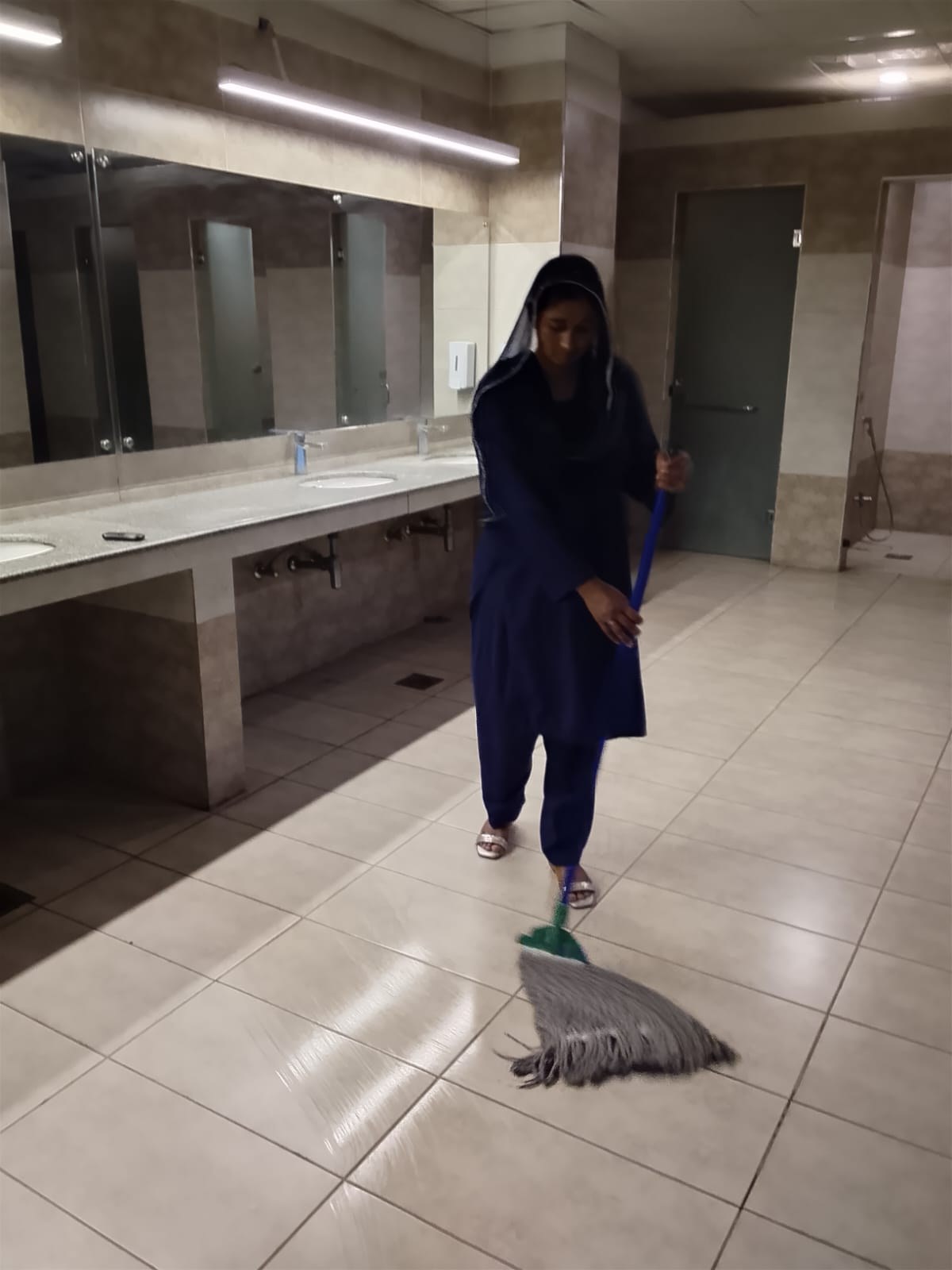 EHAS worker mopping tiled floor inside a facility washroom